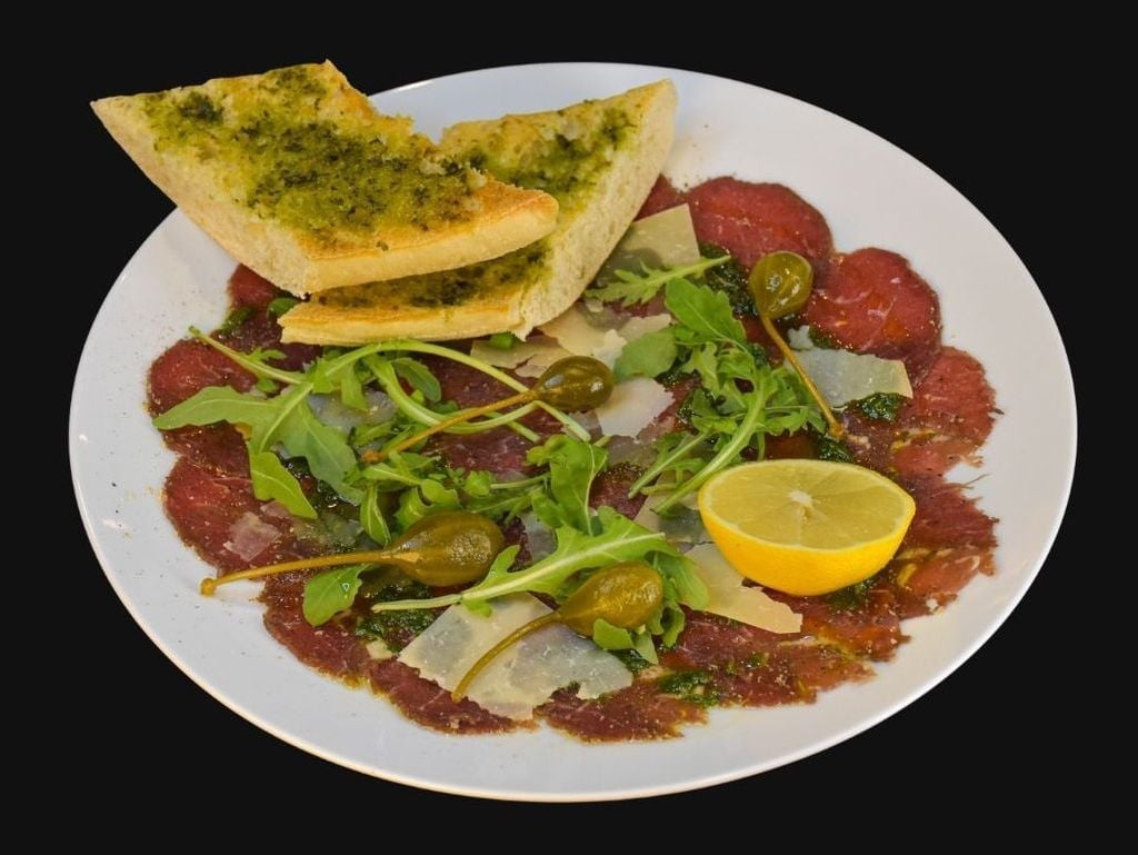 Hovězí carpaccio s bazalkovým pestem, rukolou, kapary a hoblinkami parmezánu