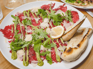 Hovězí carpaccio s hoblinami parmezánu, čerstvou rukolou a opečenou bagetou